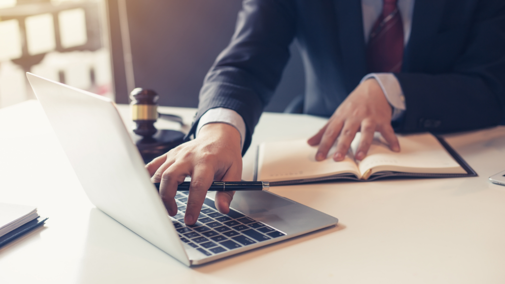 Business man writing a brief on laptop with one hand and other hand in an open book.