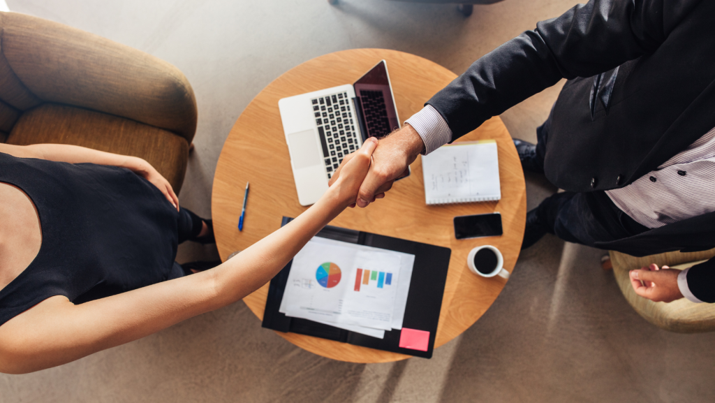 Handshake over table with laptop and documents representing a business changing hands
