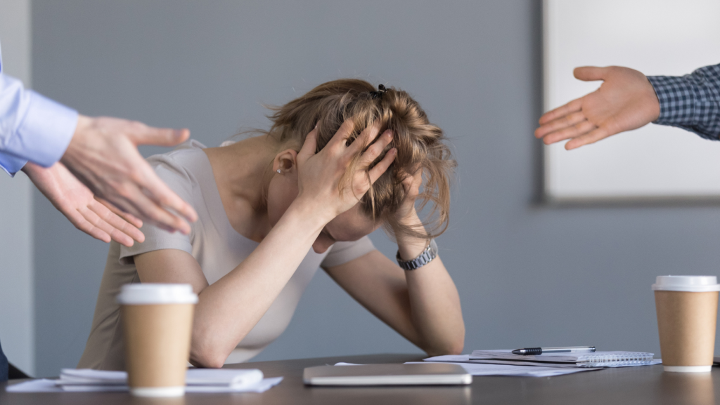 Woman with head in hands being bullied by two other figures out of shot representing an employee making stop bulling orders