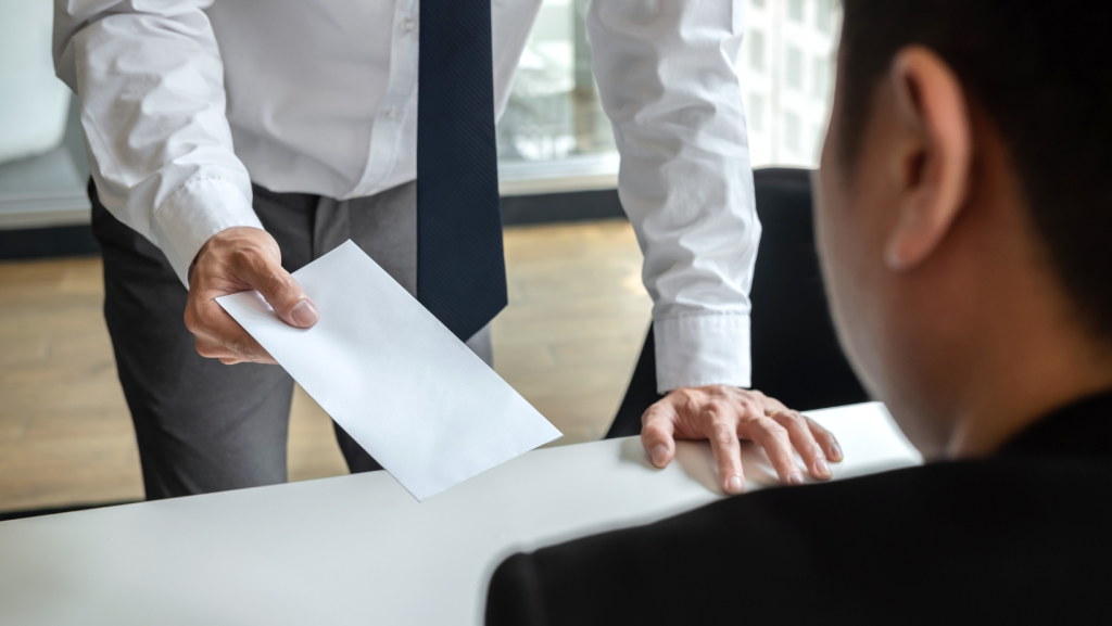Closeup of man's hand handing a white envelope containing his resignation to another man with his back to the camera